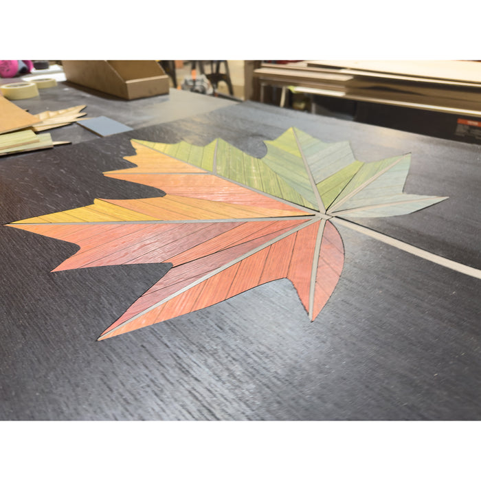 In-process shot of the Autumn Maple Leaf wall art featuring vibrant red, orange, and green tones on a black background during assembly in a workshop.